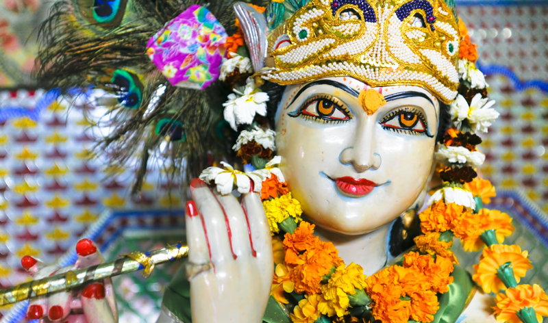 Statue of garlanded Hindu god Krishna playing flute in Delhi India